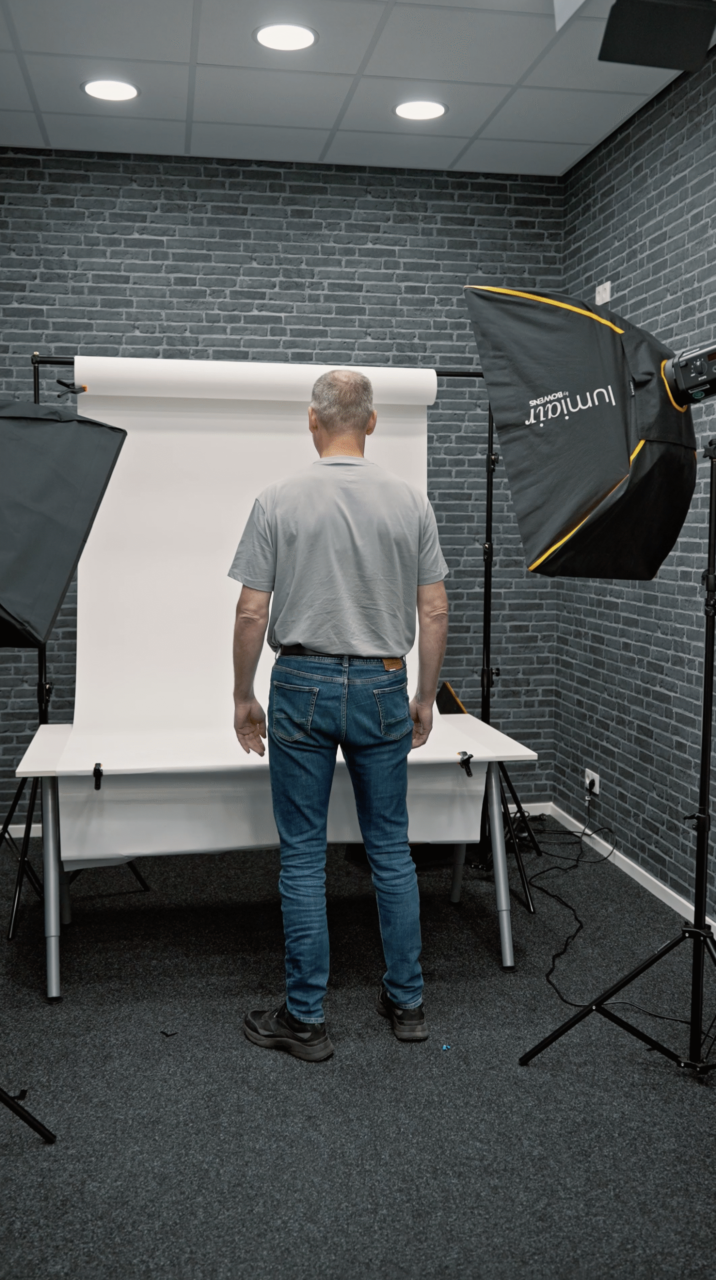 Mann im Fotostudio vor weißem Hintergrund, Blitzlichter sichtbar.